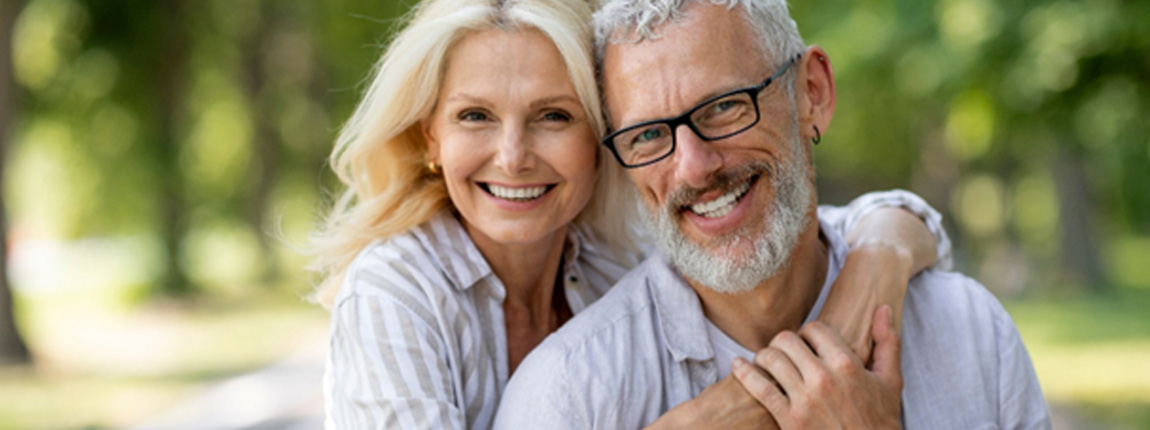 Smiling senior woman hugging smiling senior man from side