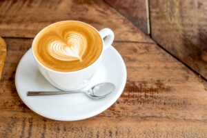Cup of coffee with a cream foam design on a white saucer on a wooden table